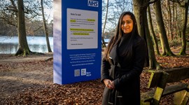 Harmeet stands in front of the NHS Talking Therapies public display in Black Park