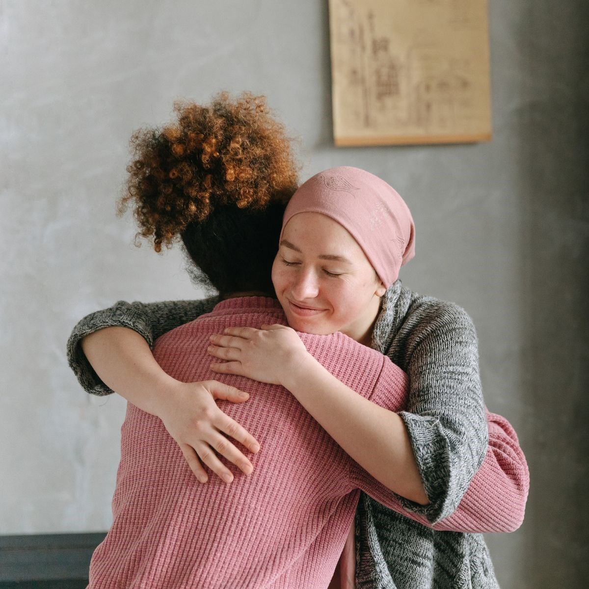 Two women embrace, the woman facing the camera is wearing a head covering and looks relieved
