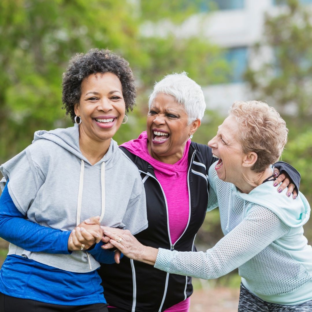Three older women laughing together whilst outside doing exercise 