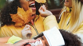 Two people dressed in autumnal clothes, holding orange leaf. Person at bottom of image is laid in bed with flu