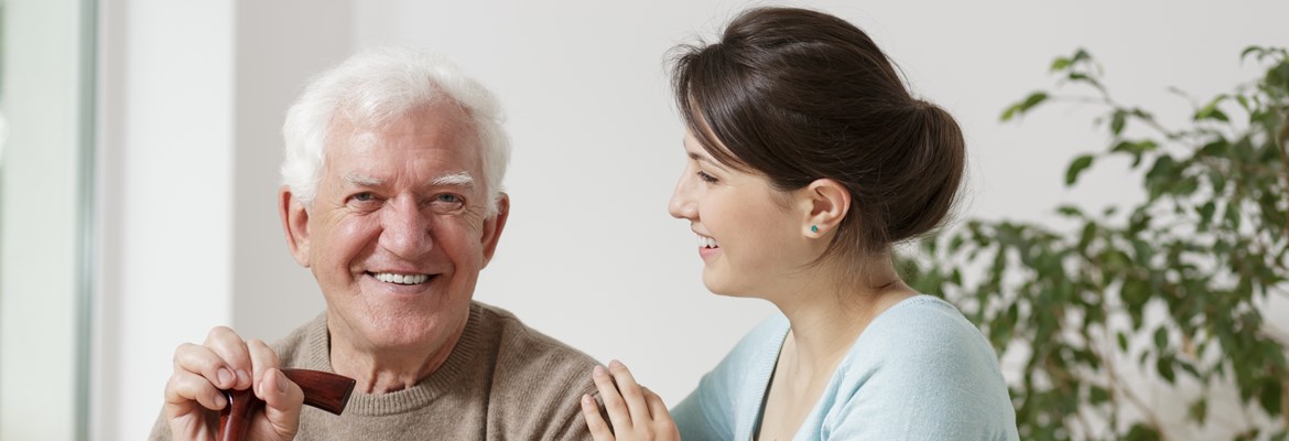 Elderly man looking content, sitting with a younger female carer