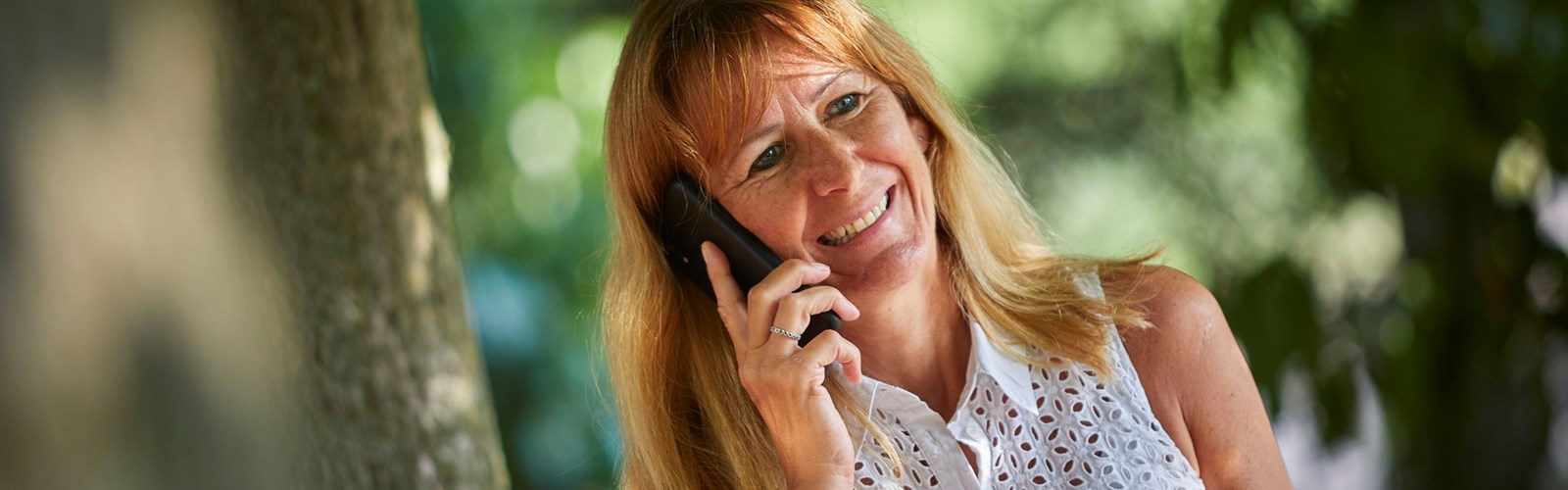 Happy woman stands in a park talking into a mobile phone